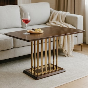 May include: A rectangular, dark wood side table with a gold metal base. The table is set with a glass of red wine and a small plate of food. The table is in front of a light-colored sofa.