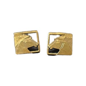 May include: A pair of gold-coloured cufflinks featuring a horse head design. Each cufflink has a square frame with a horse profile and a black background. The cufflinks are likely made of metal.