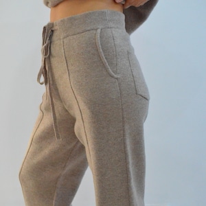 Op de afbeelding: Lichtbruine gebreide joggingbroek met een tailleband met trekkoord en zijzakken. De broek heeft een relaxte pasvorm en is gemaakt van een zacht, comfortabel materiaal. De broek maakt deel uit van een bijpassende set.