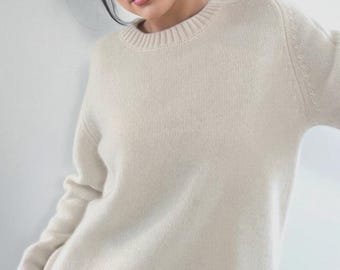 May include: Cream-colored sweater with a ribbed hem and cuffs. The long-sleeved knitwear has a crew neck and a simple, classic design. The sweater is made of a soft, possibly wool or cashmere material, and is suitable for casual wear.