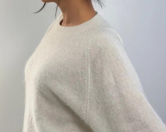 May include: A cream-coloured crew neck jumper with long sleeves. The jumper has a soft, textured appearance and a ribbed neckline. The model has dark hair tied up and is wearing small earrings.