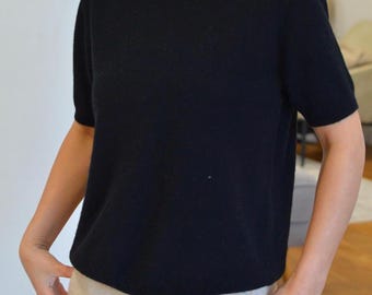 Könnte beinhalten: Ein kurzärmeliger schwarzer Strickpullover mit Rundhalsausschnitt und geradem Saum. Das Kleidungsstück ist aus einem weichen, fein gestrickten Material gefertigt und weist eine durchgehend einheitliche schwarze Farbe am Rumpf und an den Ärmeln auf.