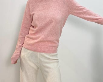 May include: A light pink crew neck sweater with long sleeves. The sweater is paired with off-white wide-leg pants. The outfit is simple and casual, suitable for everyday wear. The sweater's color is soft and muted.
