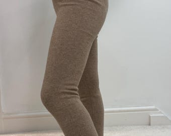 May include: A light brown two-piece matching set, comprising leggings and a long-sleeved top. The leggings are close-fitting and reach the ankles. The top has a crew neck and long sleeves. The outfit is made of a soft, knitted material.