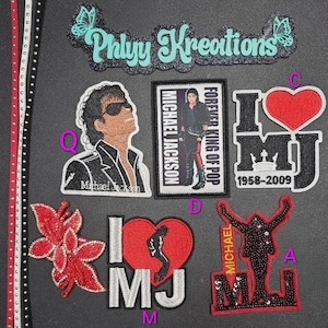 May include: A collection of embroidered patches featuring Michael Jackson imagery, including a portrait, a rectangular label, heart-shaped designs with the text I LOVE MJ, and a silhouette figure, alongside a Phlyy Kreations logo and decorative trim.