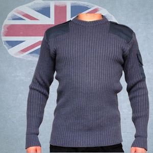 Może przedstawiać: Granatowy sweter z prążkowanej dzianiny ze wzmocnionymi naszywkami na ramionach i małą kieszenią na lewym rękawie. Sweter ma okrągły dekolt i długie rękawy. Tło przedstawia wyblakłą flagę brytyjską.