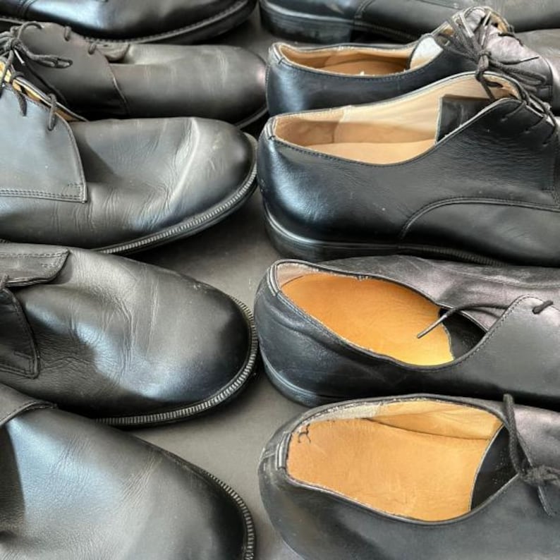 May include: A collection of black leather dress shoes with laces. The shoes are arranged closely together, showcasing their classic design and polished appearance. Some shoes have visible insoles.