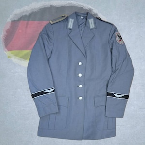 Può includere: Una giacca in stile militare grigia con risvolto dentellato, quattro bottoni color argento e due tasche inferiori. Le spalle hanno spalline, il colletto mostra linguette rettangolari argentate e le maniche presentano fasce nere con emblemi alati bianchi.