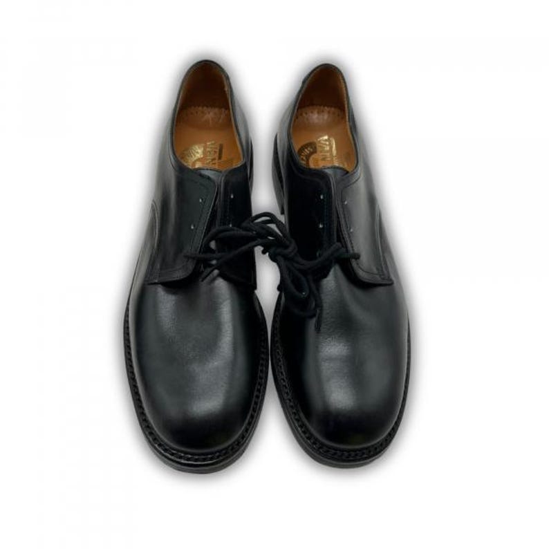 May include: A pair of black leather dress shoes with laces. The shoes have a classic design with a rounded toe and a low heel. The soles are black and have a textured pattern. The shoes are displayed on a white background.