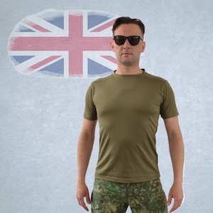 Könnte beinhalten: Eine Person trägt ein kurzärmeliges olivgrünes T-Shirt und eine Camouflage-Hose mit schwarzer Sonnenbrille. Im Hintergrund ist eine verblasste Union-Jack-Flagge zu sehen.