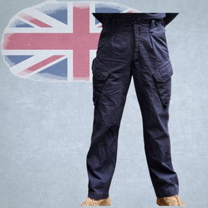 Könnte beinhalten: Marineblaue Cargohose mit mehreren Taschen und hohem Bund. Die Hose hat eine lockere Passform und ist aus strapazierfähigem Stoff gefertigt. Im Hintergrund ist eine verblasste Union-Jack-Flagge zu sehen.