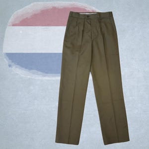 Può includere: Pantaloni verde oliva con chiusura a bottone e pieghe. I pantaloni hanno un design a gamba dritta e sono realizzati in un tessuto a tinta unita. I pantaloni sono esposti su uno sfondo azzurro e bianco.