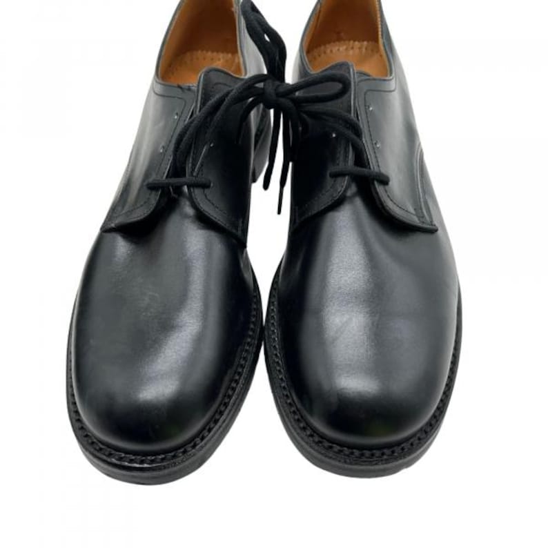 May include: A pair of black leather dress shoes with black laces. The shoes have a rounded toe and a stitched sole. The shoes are displayed on a white background.