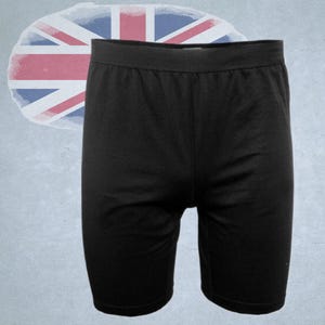 Könnte beinhalten: Schwarze Radlerhose mit elastischem Bund. Die Shorts sind knielang und aus einem einfarbigen, dunklen Stoff gefertigt. Im Hintergrund befindet sich eine Union-Jack-Flagge.
