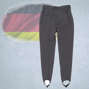 Könnte beinhalten: Dunkelgraue Steg-Hose mit zwei Reißverschlusstaschen und weißen Steg-Riemen. Die Hose ist aus einem glatten Stoff gefertigt und hat eine maßgeschneiderte Passform. Der Hintergrund enthält eine verblasste deutsche Flagge.