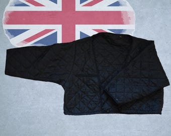 May include: A black quilted jacket with a V-neckline and long sleeves, featuring a diamond-stitched pattern throughout the fabric. The jacket is positioned in front of a large, circular graphic depicting the Union Jack flag in red, white, and blue.