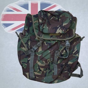 Puede incluir: Una mochila con estampado de camuflaje que cuenta con una solapa superior con dos cierres de hebilla de plástico, correas ajustables y el texto "FORZA 33" impreso en el frente. La bolsa muestra un patrón en verde, marrón y negro.