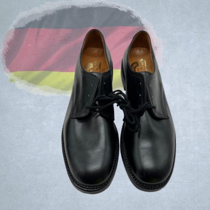 May include: A pair of black leather dress shoes with laces. The shoes have a rounded toe and a stitched sole. The background features a stylized German flag.