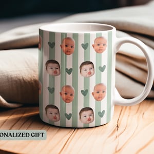 May include: White ceramic mug featuring a pattern of baby faces and green hearts on a striped background. The mug has a white handle and the text "PERSONALIZED GIFT" is visible.
