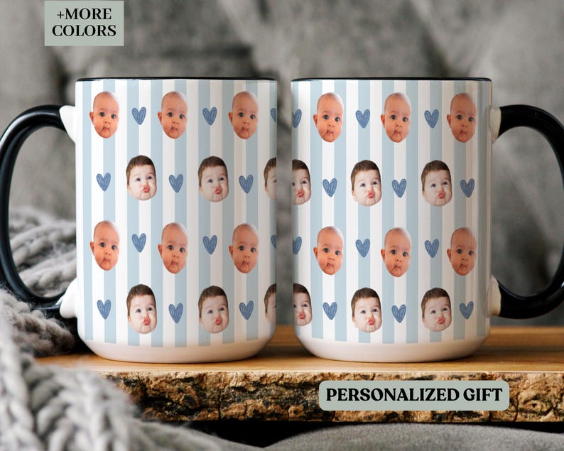 May include: Two white ceramic mugs with black handles and rims. The mugs display a pattern of baby faces, blue hearts, and vertical blue stripes. The text "+MORE COLORS" and "PERSONALIZED GIFT" are visible.