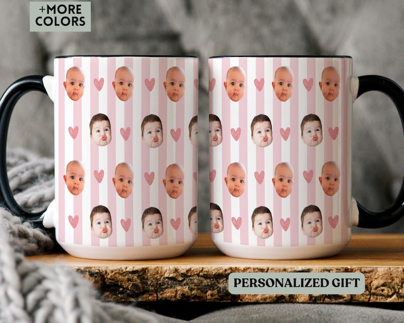 May include: Two white ceramic mugs with black handles. The mugs have a repeating pattern of baby faces, pink hearts, and pink and white stripes. The text "PERSONALIZED GIFT" is visible on the bottom of the mug.