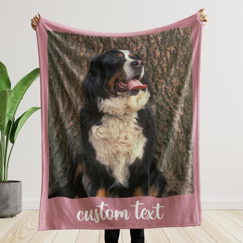 May include: A pink blanket featuring a Bernese Mountain Dog with a tree bark background. The dog has black, white, and brown fur, with its tongue sticking out. The words "custom text" are written in white script at the bottom.