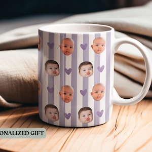 May include: White ceramic mug featuring a pattern of baby faces and purple hearts on a striped background. The mug has a large handle and the text "PERSONALIZED GIFT" is visible.