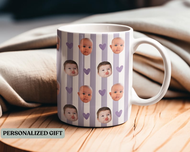 May include: White ceramic mug featuring a pattern of baby faces and purple hearts on a striped background. The mug has a large handle and the text "PERSONALIZED GIFT" is visible.