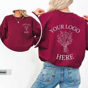 May include: Maroon sweatshirt with white text and floral design. The front of the sweatshirt has the text "YOUR LOGO HERE" and a floral design. The back of the sweatshirt has the same text and design.