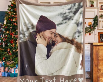 May include: A personalized blanket featuring a couple in a winter scene. The blanket has a brown border and the text "Your Text Here" with a heart. The couple is smiling and wearing winter clothing.
