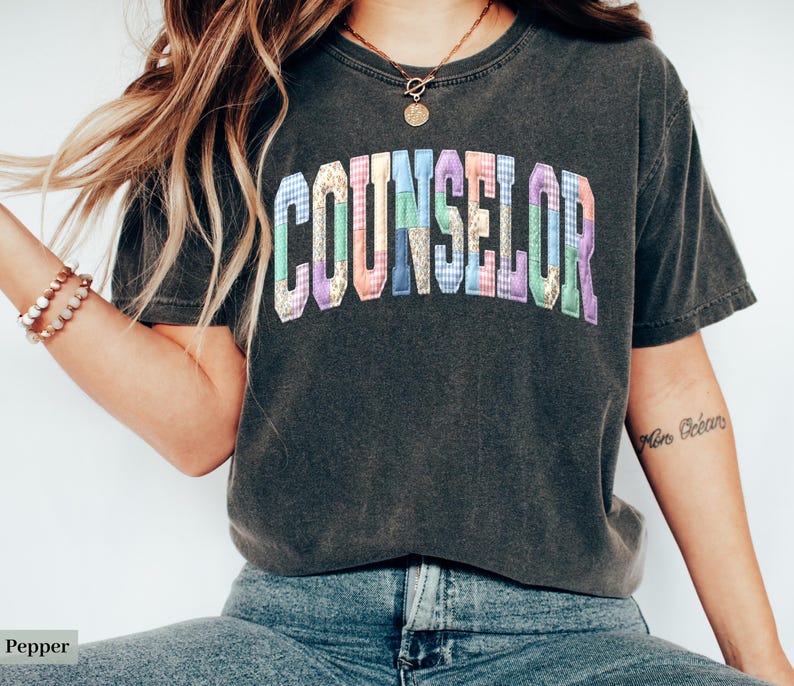 Peut inclure: T-shirt gris fonc&eacute; avec le mot "COUNSELOR" en lettres patchwork color&eacute;es. Le t-shirt a un aspect vintage et est fait d'une mati&egrave;re douce. Le design est centr&eacute; sur la poitrine.