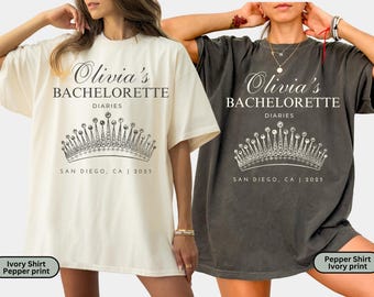 May include: Ivory and pepper-colored t-shirts with the text "Olivia's Bachelorette Diaries" and a crown graphic. The text "San Diego, CA | 2025" is printed below the crown. The shirts are short-sleeved and have a relaxed fit.
