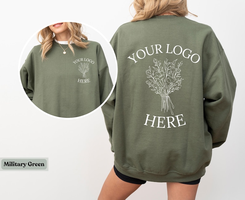 May include: Military green sweatshirt with a crew neck. The front features a small graphic and the text "YOUR LOGO HERE". The back displays a larger floral design and the same text. The sweatshirt is a solid color.