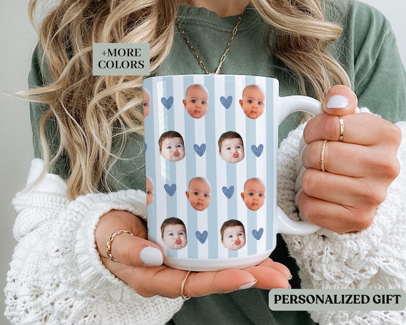 May include: A white ceramic mug with a blue and white striped design, decorated with baby faces and blue heart motifs. The mug has the text "PERSONALIZED GIFT".