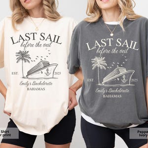 May include: Two t-shirts with a graphic design of a cruise ship and palm trees. The text on the shirts reads "Last Sail Before the Veil" and "Emily's Bachelorette Bahamas". One shirt is ivory with a pepper print and the other is pepper with an ivory print.