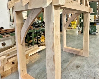 May include: A wooden porch canopy with a triangular roof and a rectangular frame. The canopy is made of unfinished wood and is in a workshop setting.