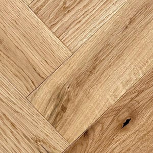 May include: Close-up of a herringbone pattern wood floor. The wood planks are a light brown color with visible grain and knots. The planks are arranged in a diagonal, zig-zag pattern, creating a textured surface. This flooring is suitable for home decor.