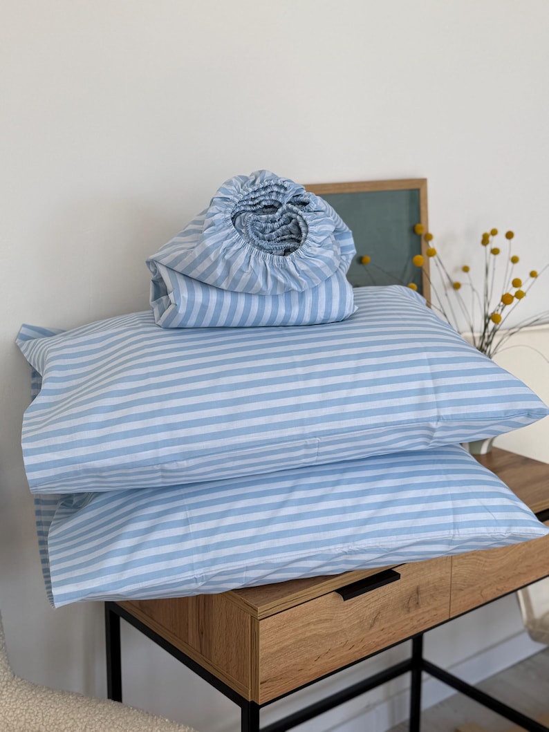 a wooden dresser with two blue and white striped pillows stacked on top of each other. There is also a folded blanket and a vase of yellow flowers on the dresser.
