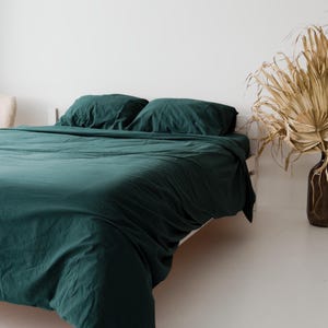 May include: A bed featuring a deep forest green duvet cover and two matching rectangular pillows. The bedding has a soft, matte texture and is draped over a white bed frame. The fabric appears lightweight and covers the entire mattress surface.