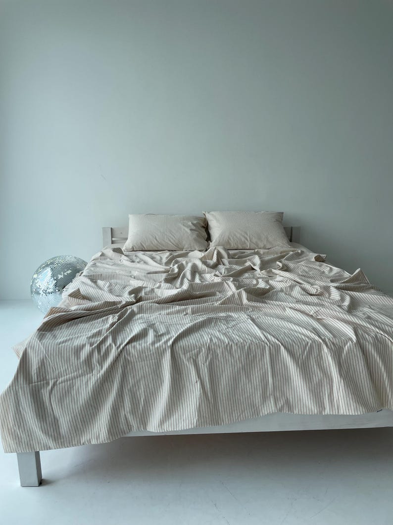 a bed with a white bedspread and pillows, and a silver disco ball is placed on the floor next to the bed.