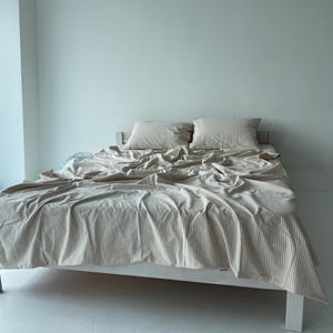 a bed with a white and gray striped comforter and pillows, set against a plain white wall.