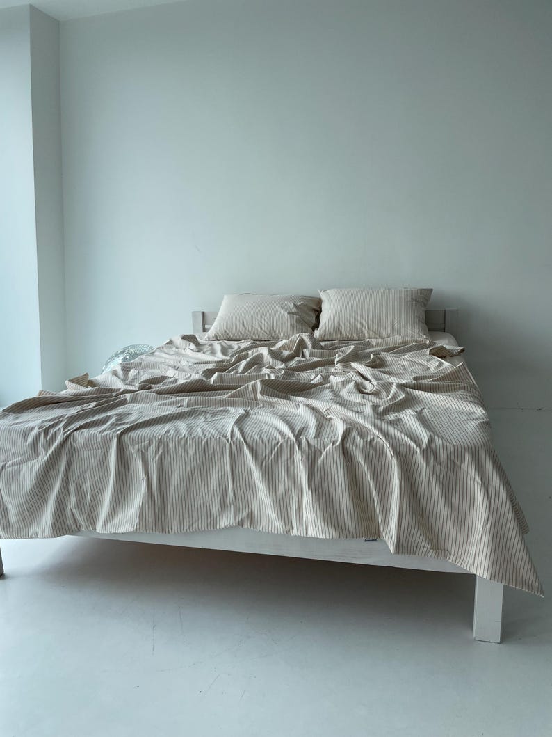 a bed with a white and gray striped comforter and pillows, set against a plain white wall.
