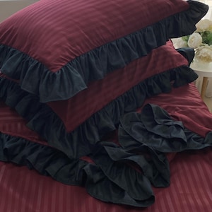 a bed with a red and black striped comforter and matching pillows, with a vase of white flowers on the windowsill.