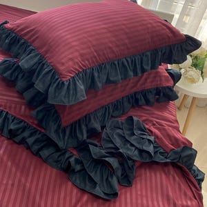 a bed with a red and black striped comforter and matching pillows, along with a small table with a vase of flowers.