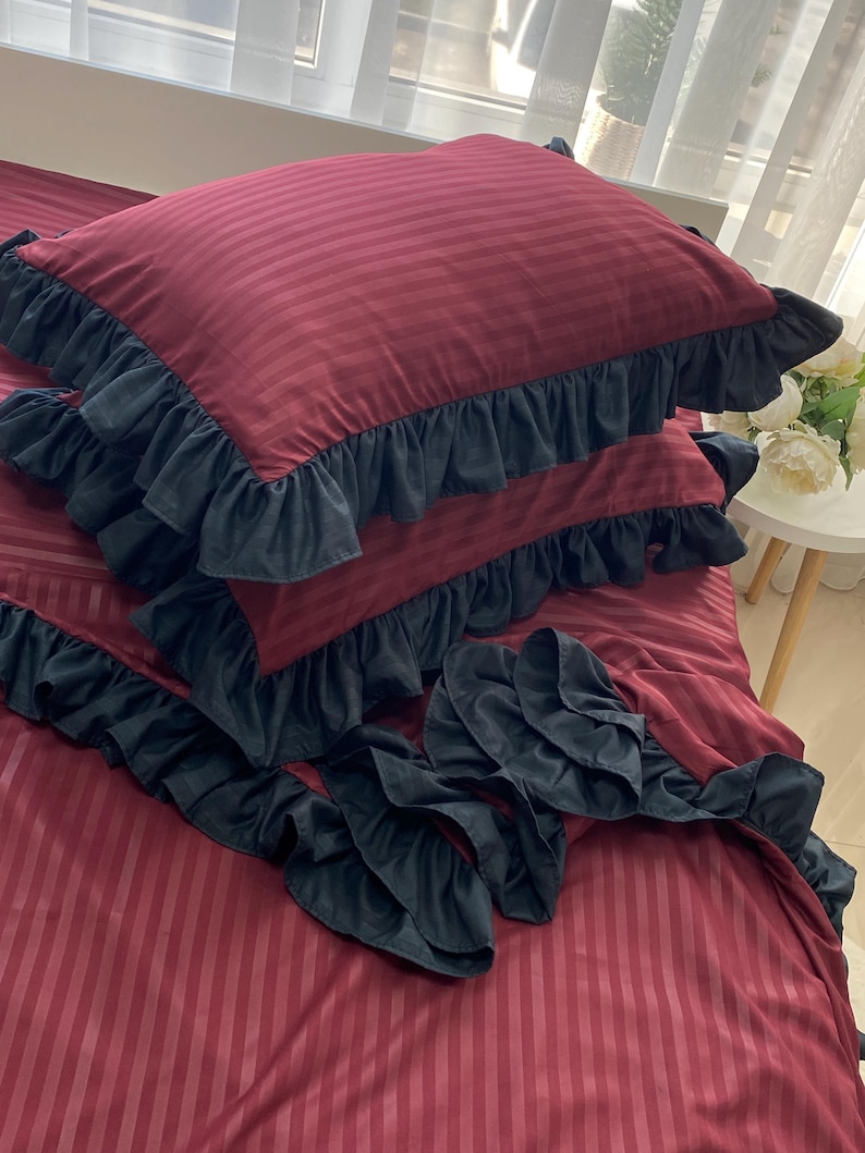 a bed with a red and black striped comforter and matching pillows, along with a small table with a vase of flowers.