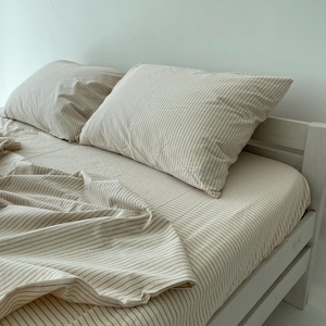 a neatly made bed with a white and beige striped comforter and two pillows.