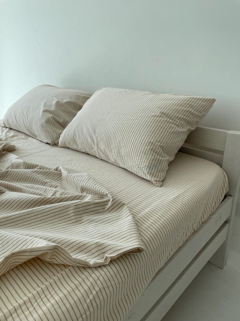 a neatly made bed with a white and beige striped comforter and two pillows.
