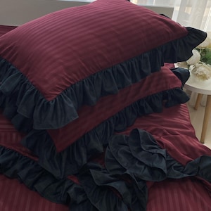 a bed with a red and black striped comforter and matching pillows, along with a small table and a vase of flowers.