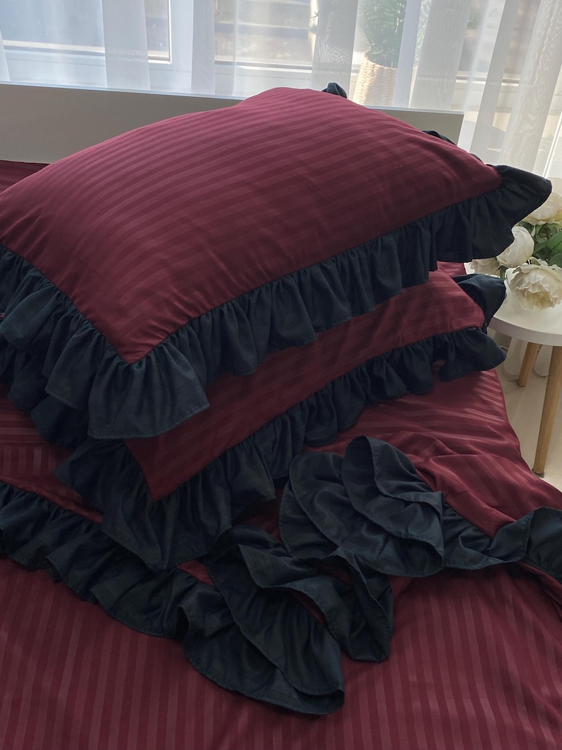 a bed with a red and black striped comforter and matching pillows, along with a small table and a vase of flowers.