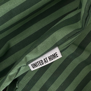 A close-up view of a green and black striped fabric with a white label that reads "UNITED AT HOME".